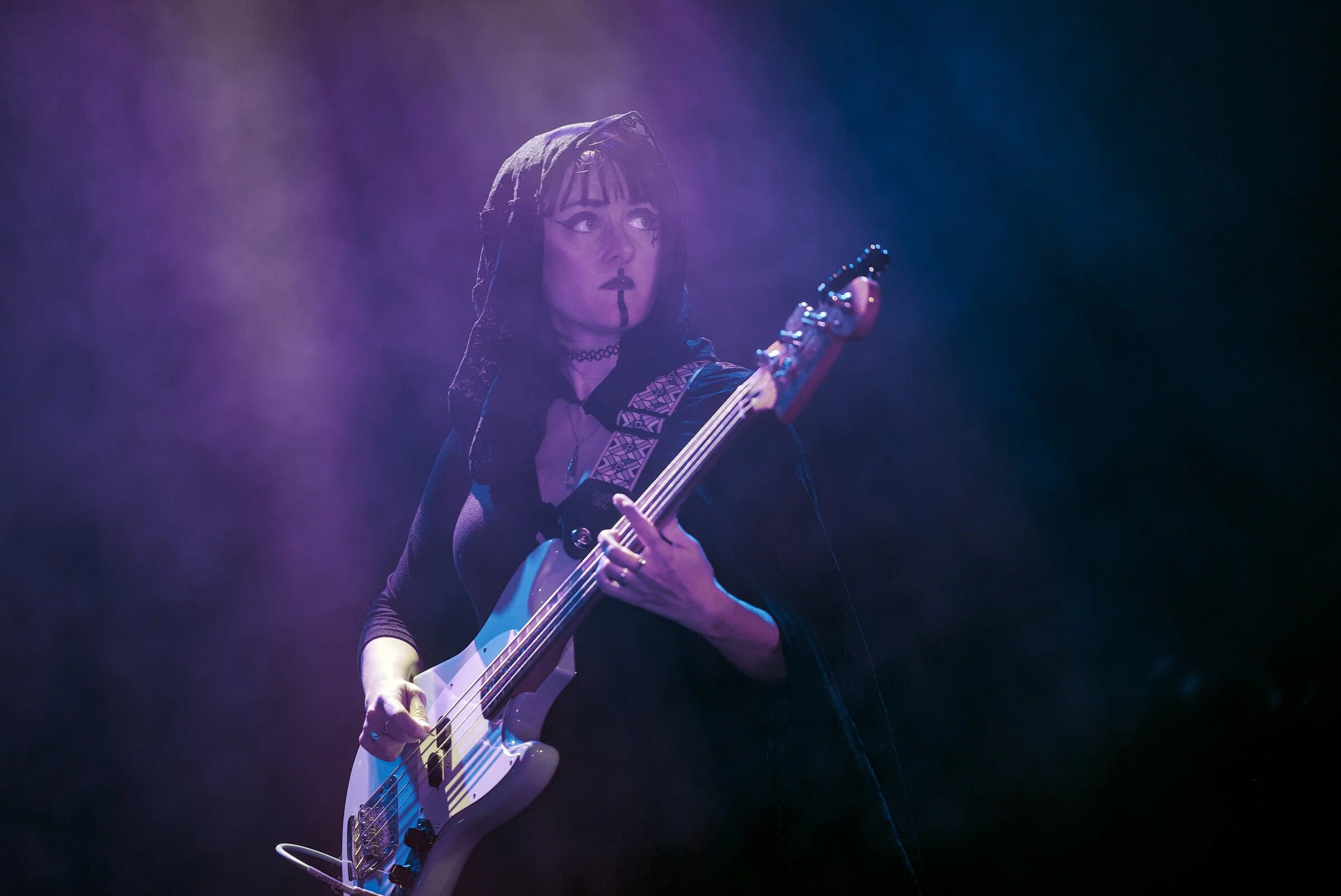 Bassiste voilée sur scène, lumière violette